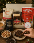 Luxury Christmas letterbox gift hamper for him featuring fruit cake, Christmas pudding popcorn, English Breakfast tea, sweet chilli peanuts and cashews, Christmas chutney and artisan dark chocolate in a premium Hallby festive gift box.