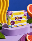 A bar of soap from the brand Edit Five, specifically a Pink Grapefruit scent, displayed on a purple pedestal. The packaging is yellow and white with purple and green floral graphics. Nan pink grapefruit soap bar, handmade in England with 100% natural essential oil and colourful gift-ready packaging—a thoughtful birthday, Christmas or Mother’s Day gift for Nan.