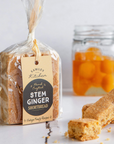 Packaged stem ginger shortbread with a jar of stem ginger in the background on a white surface.