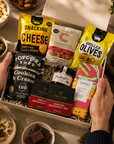 Luxury gourmet gift hamper presented in a premium magnetic gift box featuring cookies and cream popcorn, chilli jam, English Breakfast tea, grilled olives, salted caramel milk chocolate, sweet chilli peanuts and cashews, and snacking cheese.