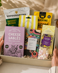 Luxury gourmet gift hamper in a premium magnetic gift box featuring lemon shortbread, cookies and cream popcorn, snacking cheese, limoncello gummies, salted caramel chocolate, red onion relish, cheese sablés and a marshmallow white hot chocolate spoon.
