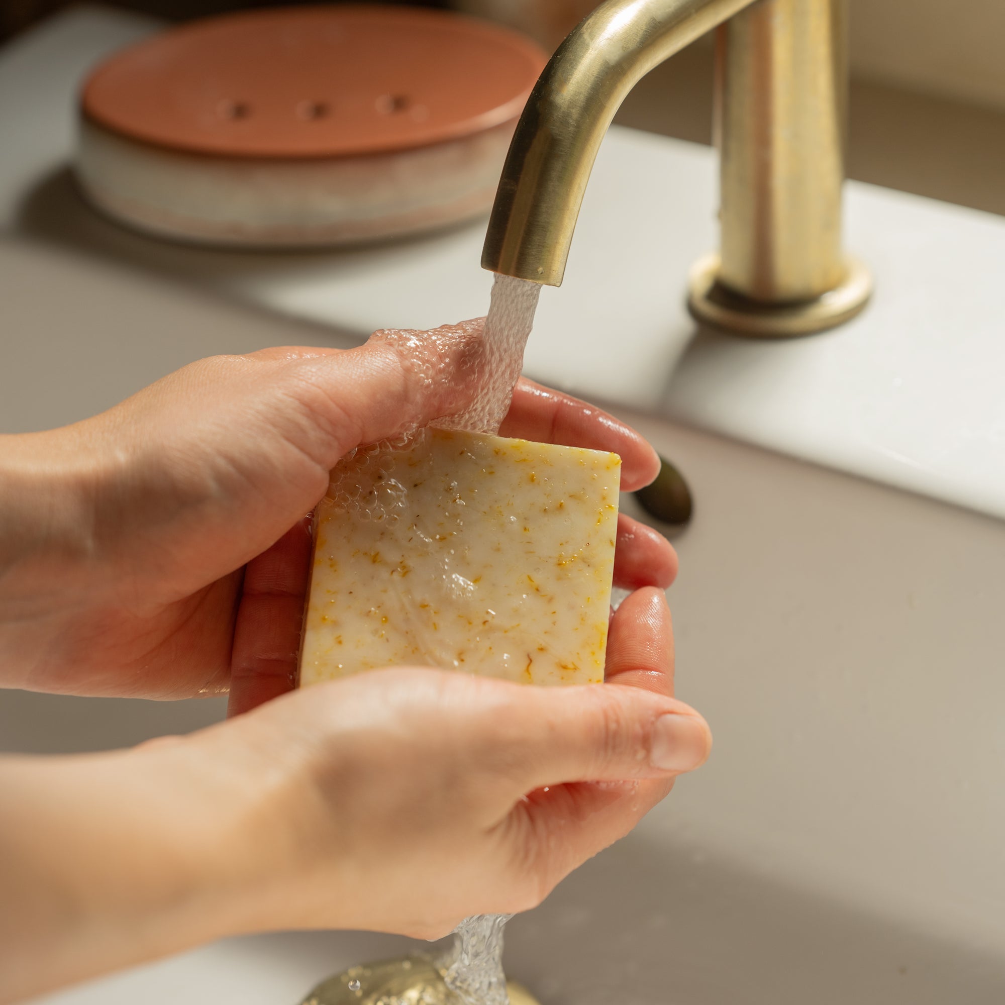 Someone washing their hands with the Energise soap bar, with scents of lemon, clementine, ylang ylang and patchouli essential oils