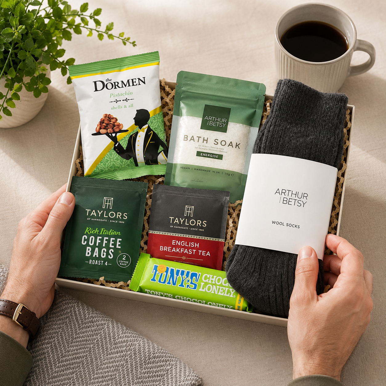 Luxury letterbox self care gift hamper for him featuring wool socks, energising bath soak, English Breakfast tea, coffee bag, pistachio nuts and Tony's Chocolonely dark almond sea salt chocolate in a premium Hallby gift box.
