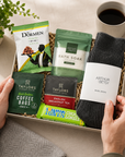 Luxury letterbox self care gift hamper for him featuring wool socks, energising bath soak, English Breakfast tea, coffee bag, pistachio nuts and Tony's Chocolonely dark almond sea salt chocolate in a premium Hallby gift box.