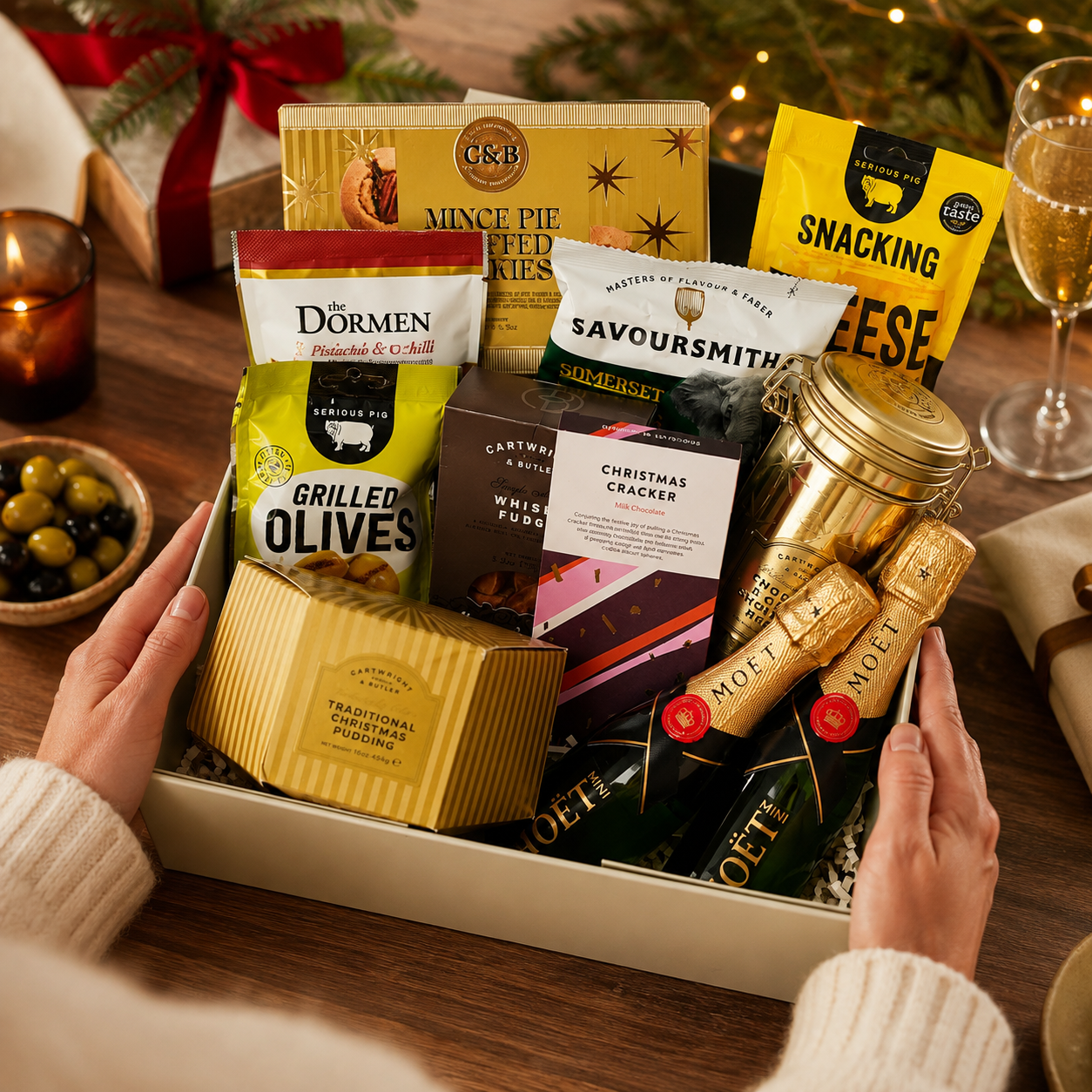 Luxury Christmas champagne gift hamper in a large magnetic gift box featuring two bottles of Moët & Chandon Champagne, Christmas chocolate, grilled olives, snacking cheese, cheddar and shallot crisps, chocolate and orange shortbread, festive nut mix, whisky fudge, mince pie stuffed cookies and Christmas pudding.
