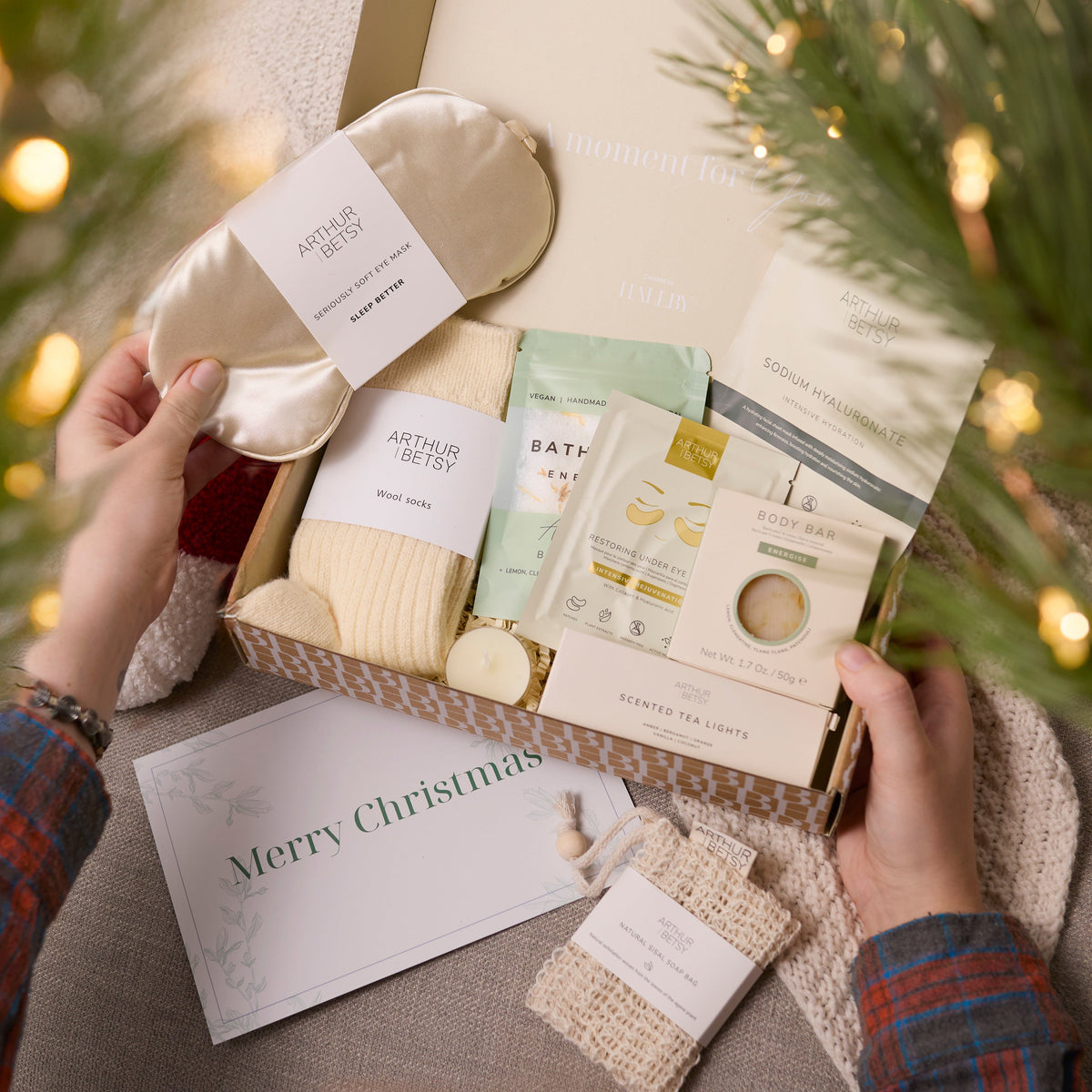 Unboxing a Hallby Christmas-themed gift set with bath products and a sleep mask, surrounded by festive decorations.
