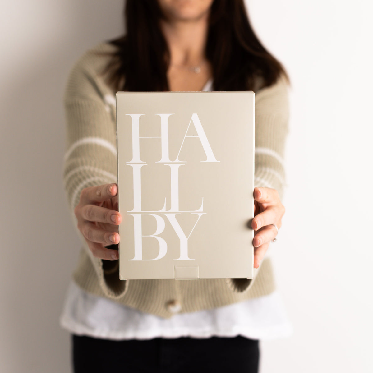Person holding a beige card with 'HAL LBY' text against a neutral background