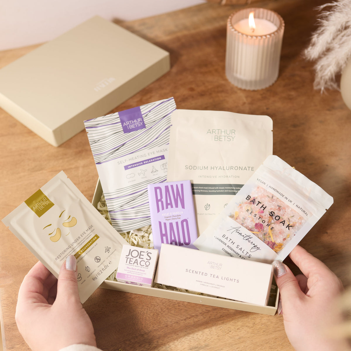 Hallby Luxury Pamper gift box being unboxed on a rustic wooden table. Box includes bath salts, candles and other self care products.