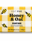 A rectangular bar of soap wrapped in a yellow and white gingham patterned paper sleeve decorated with illustrations of honey bees. The text on the wrapper reads 'EDIT FIVE Honey & Oat SOAP BAR' - Traditional honey and oat soap handmade in England—a mild artisan cleansing bar for everyday skincare, relaxing showers, bath-time rituals and thoughtful wellbeing gifts.