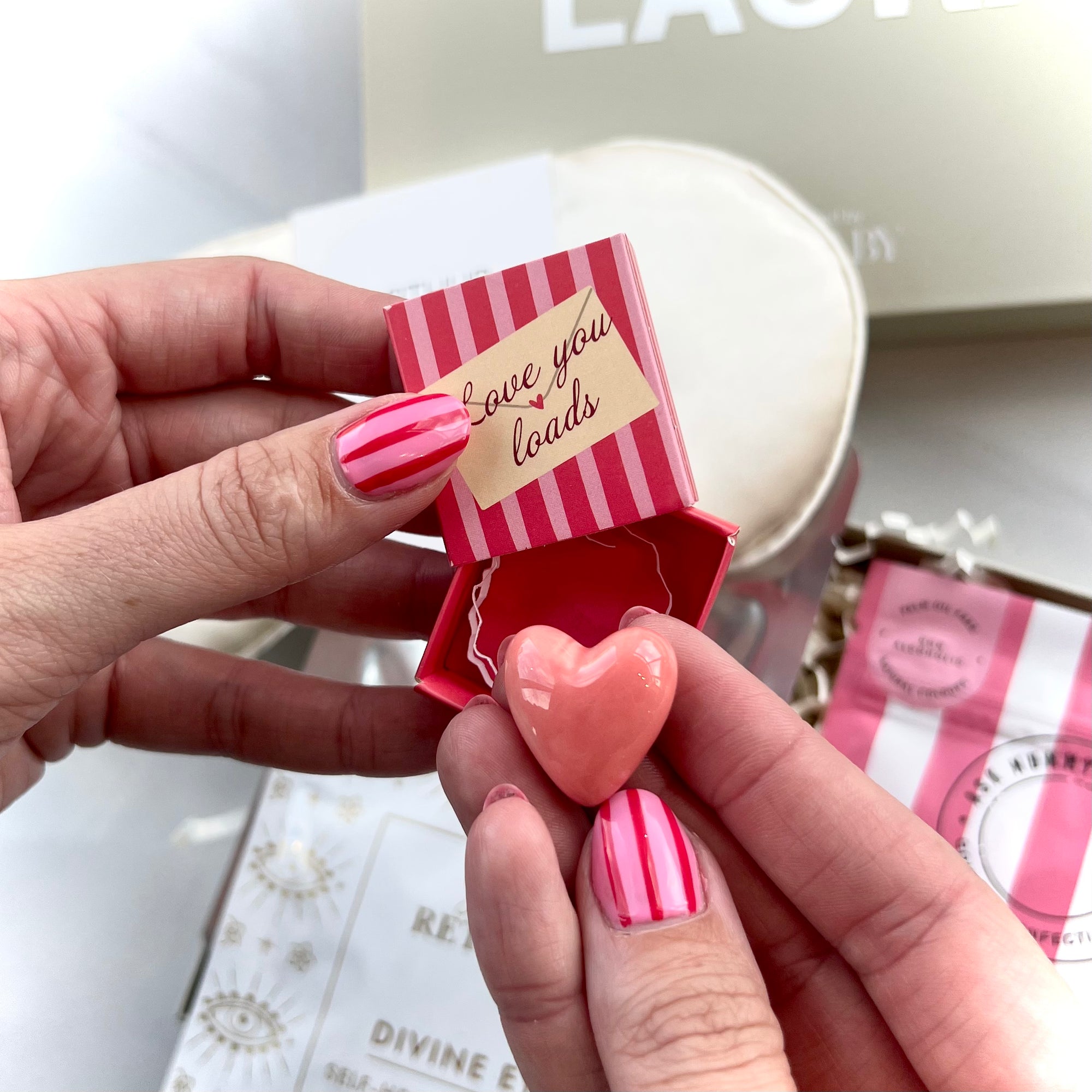 Person holding a small striped box with a heart-shaped object and 'love you loads' text.