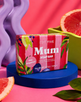 A pink grapefruit scented soap bar by Edit Five, packaged in a colorful box with botanical illustrations, displayed on a blue pedestal with grapefruit slices and a purple sculptural background. Luxury handmade soap for Mum with refreshing pink grapefruit essential oil, a rich everyday lather and colourful blush packaging, perfect for Mother’s Day and birthday gifting.