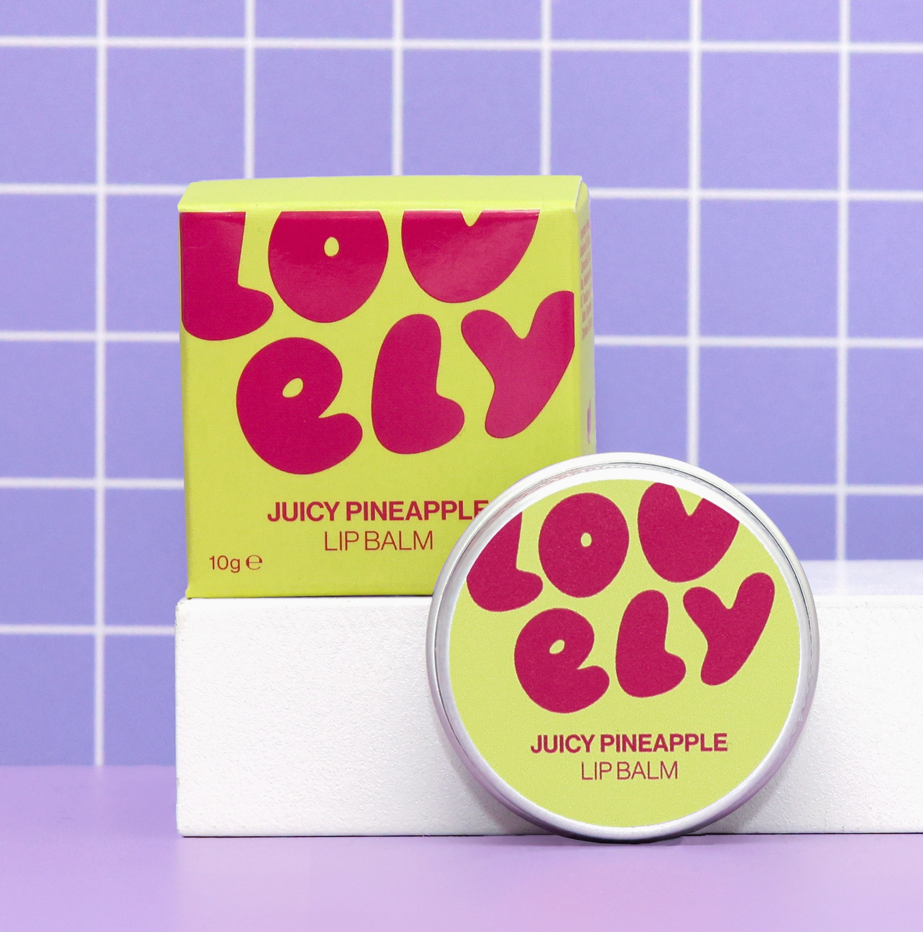 Lovely Juicy Pineapple lip balm with packaging on a purple tiled background