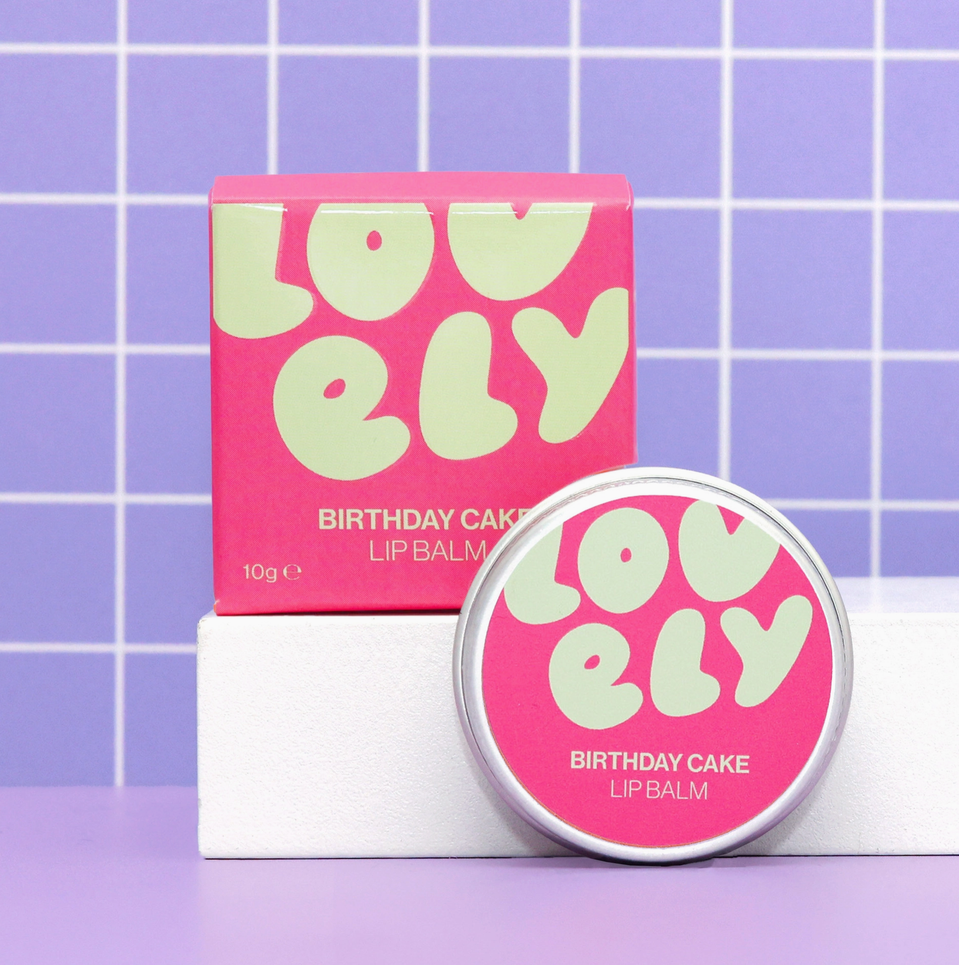 Lovelily Birthday Cake lip balm packaging on a purple grid background