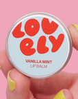 Lip balm container with 'LOVELY' branding on a pink background