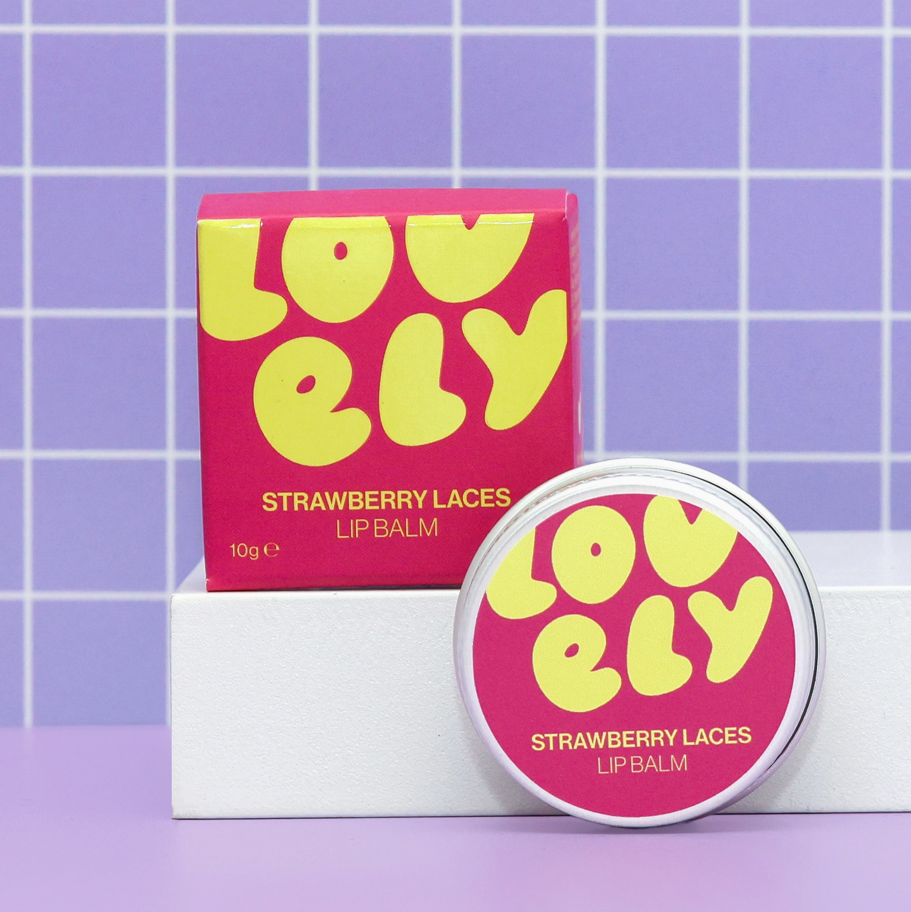 Lovely Strawberry Laces lip balm with packaging on a purple grid background