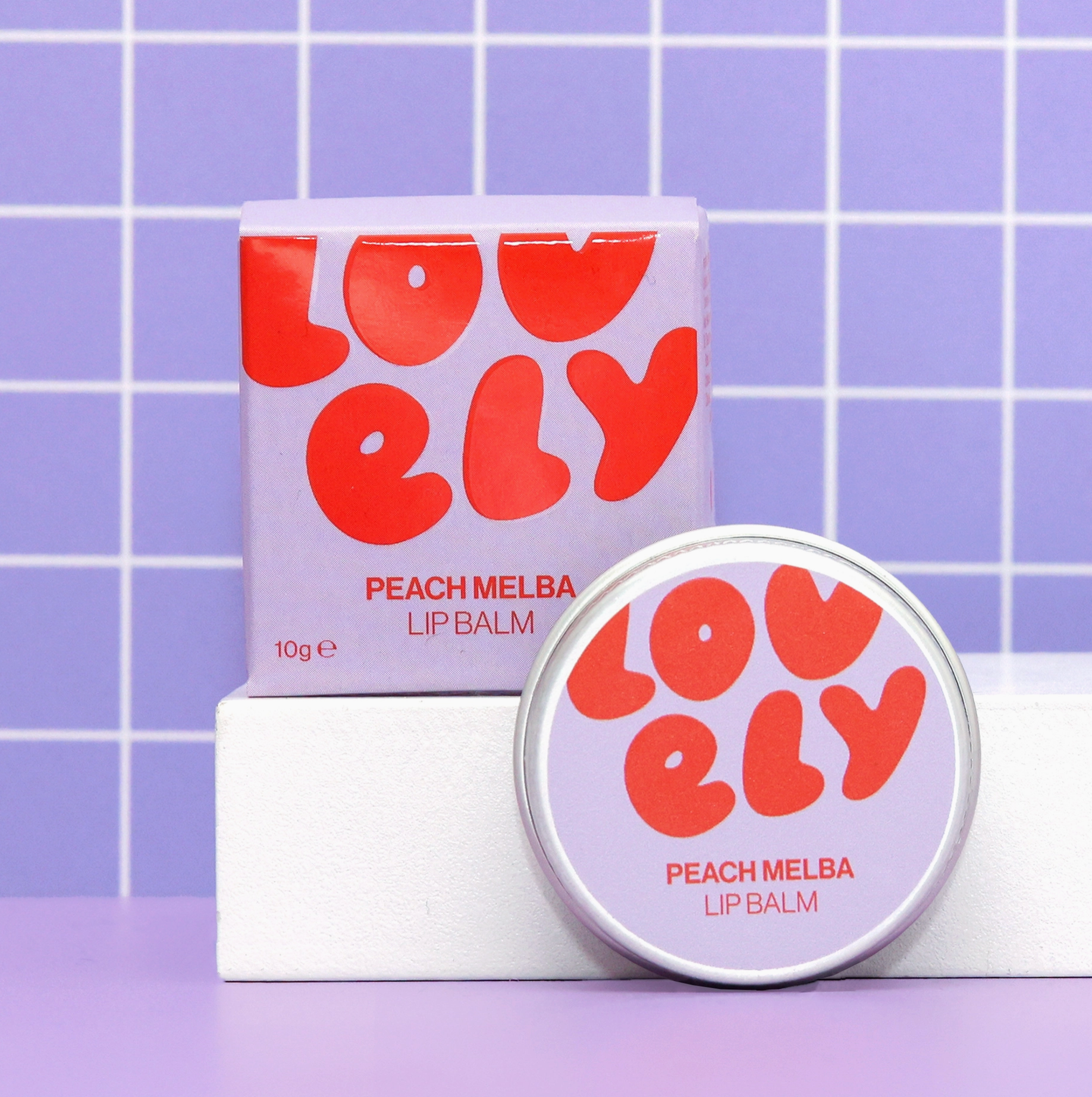 LOVELY Peach Melba lip balm with packaging on a purple tiled background