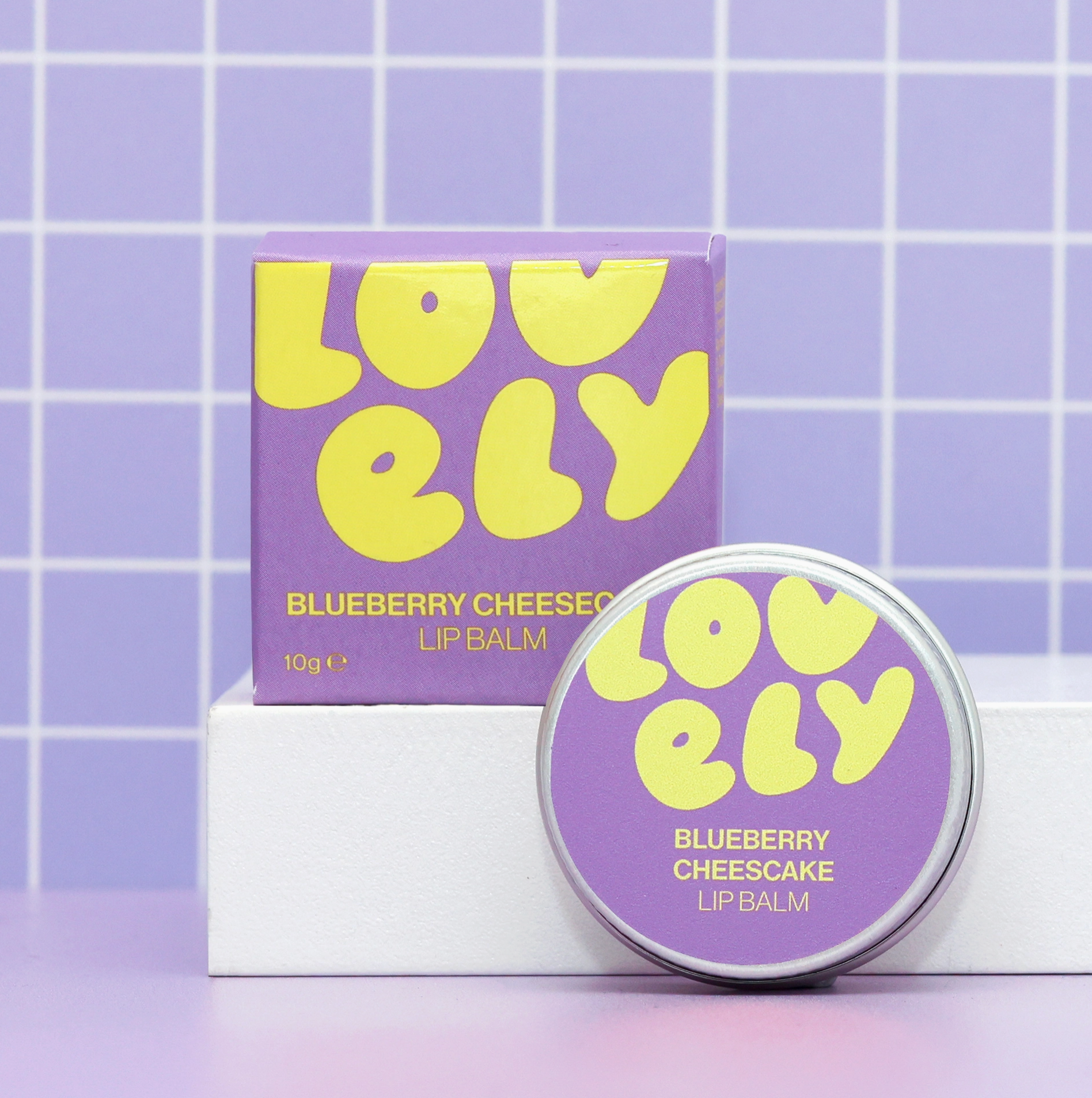 Purple and yellow lip balm with packaging on a tiled background