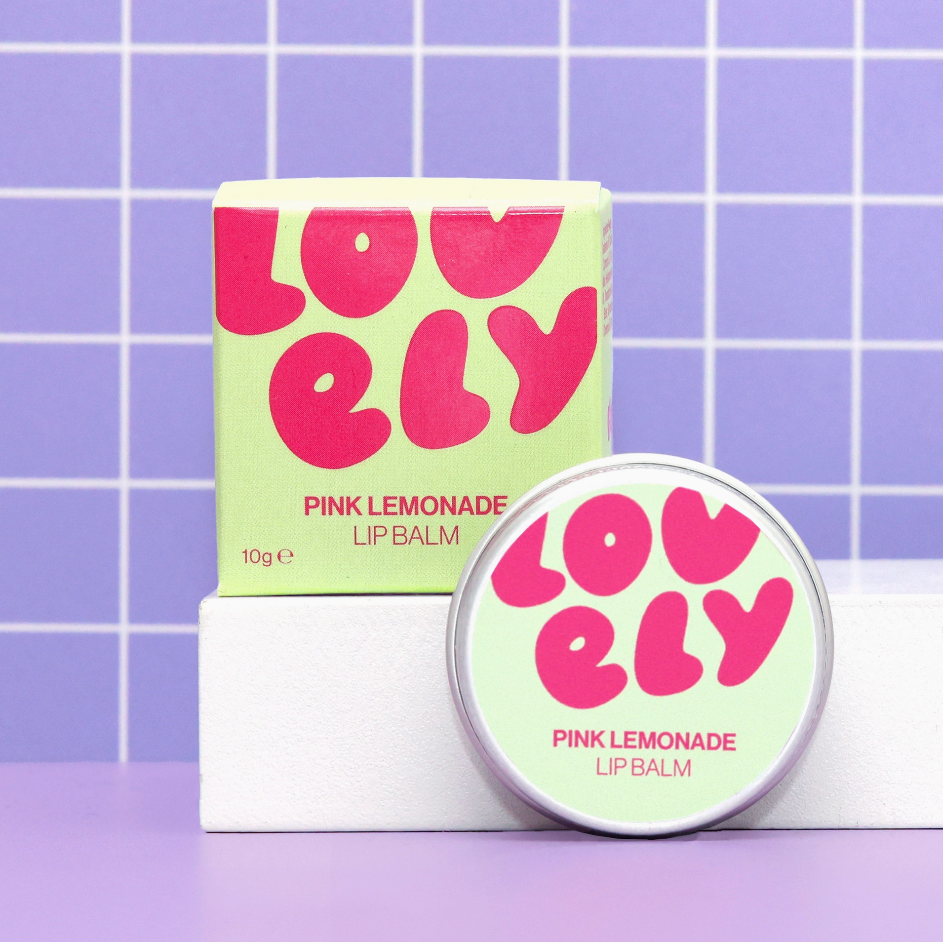 Pink Lemonade lip balm with packaging on a purple grid background