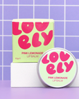 Pink Lemonade lip balm with packaging on a purple grid background