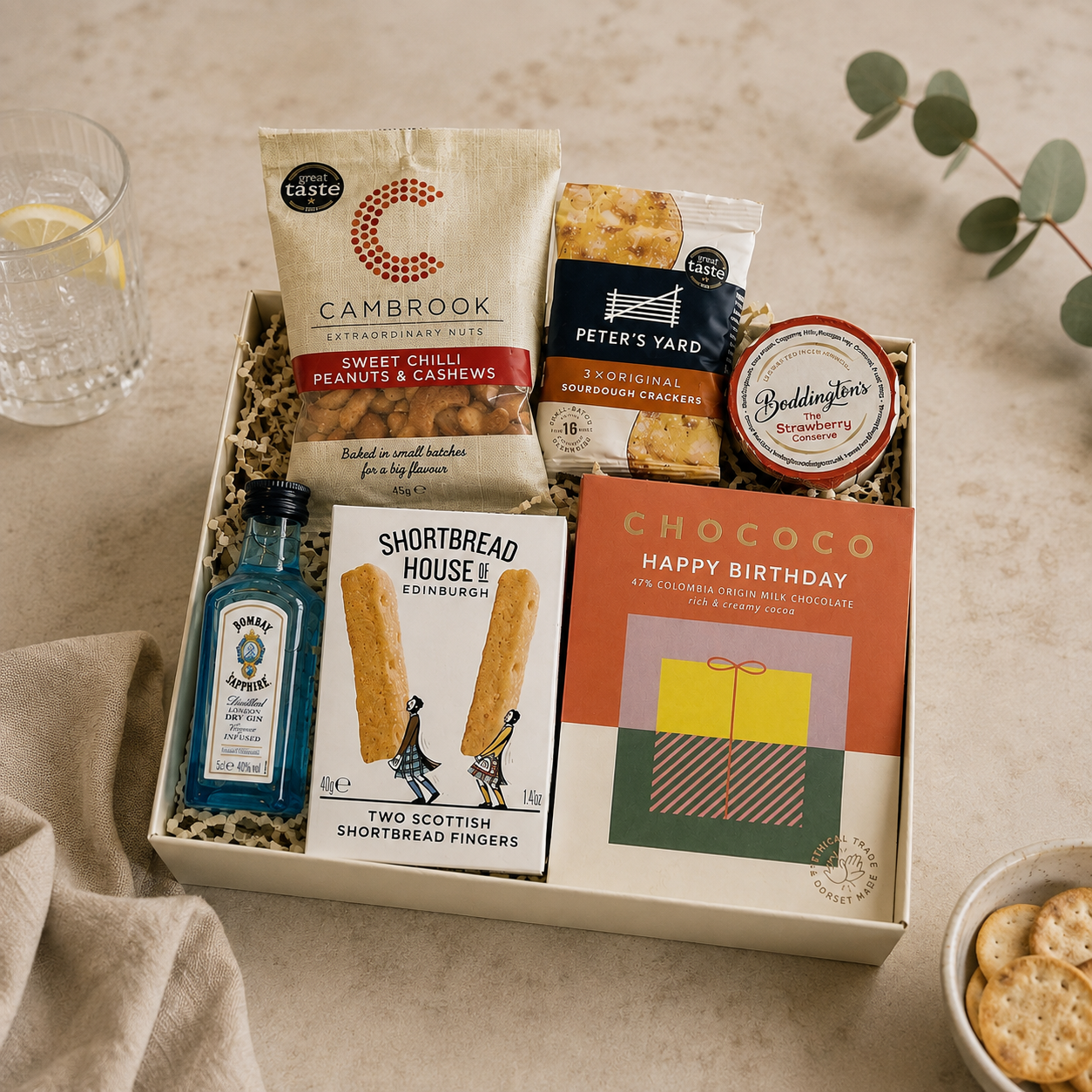 Luxury happy birthday letterbox gift hamper with birthday chocolate bar, Bombay Sapphire gin, sweet chilli peanuts and cashews, artisan shortbread, sourdough crackers and strawberry conserve in a premium Hallby gift box.