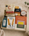 Luxury happy birthday letterbox gift hamper with birthday chocolate bar, Bombay Sapphire gin, sweet chilli peanuts and cashews, artisan shortbread, sourdough crackers and strawberry conserve in a premium Hallby gift box.