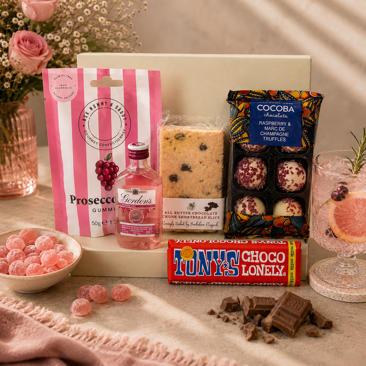 Luxury pink letterbox gift hamper featuring Gordon's Pink Gin, Prosecco Rosé gummies, Tony's Chocolonely milk chocolate, chocolate chunk shortbread slice and raspberry Marc de Champagne truffles presented in a premium Hallby gift box.