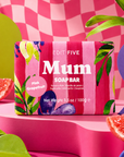 A pink striped soap bar package labeled 'EDIT FIVE Mum SOAP BAR' and 'Pink Grapefruit,' styled on a pink pedestal with grapefruit slices and colorful abstract shapes in the background. Mum pink grapefruit soap bar, handmade in England with 100% natural essential oil and blush-toned gift-ready packaging—a thoughtful Mother’s Day, birthday or Christmas gift for Mum.